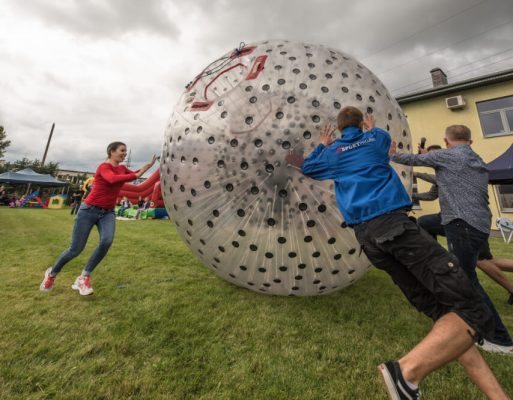 Ludzie pchają po trawie dmuchaną kulę do zorbingu.