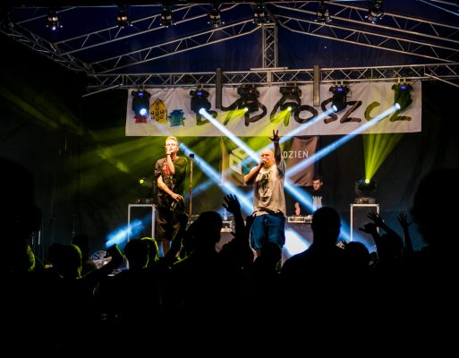 Dwóch mężczyzn występuje na scenie plenerowej.