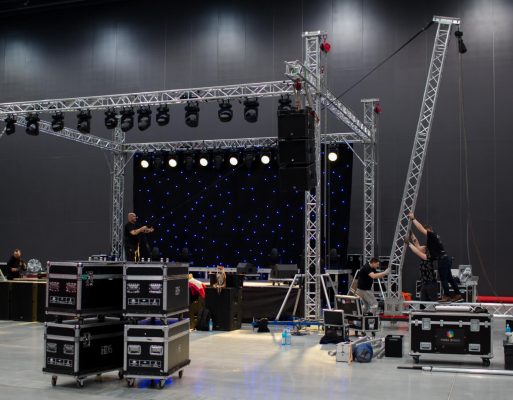 Mężczyźni montują konstrukcję sceniczną w hali wystawowej.