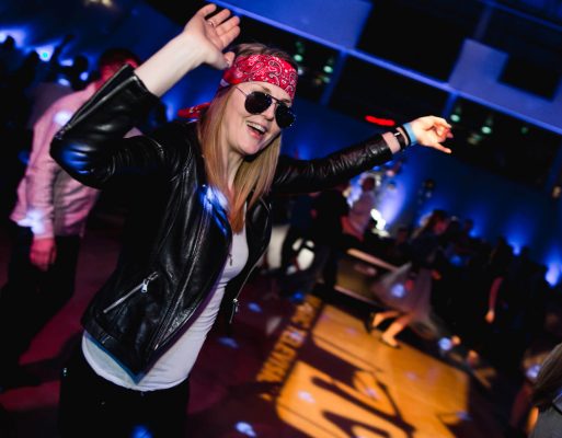 Kobieta przebrana za gwiazdę rocka tańczy na tematycznej imprezie integracyjnej.