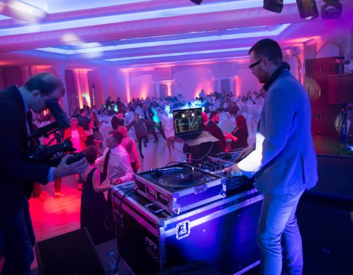 Dj stoi na scenie przy konsolecie na tle ludzi bawiących się na imprezie integracyjnej.