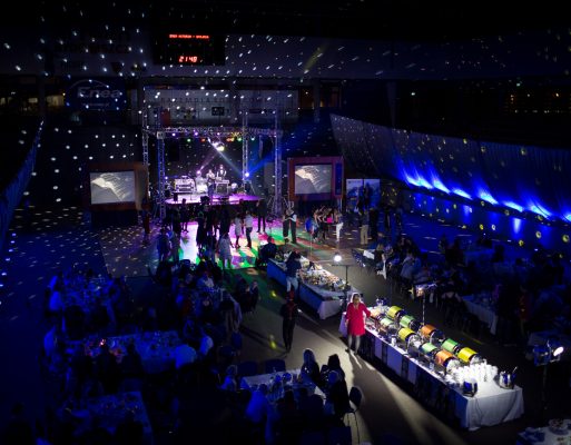Kolorowo oświetlona sala ze sceną, multimediami i cateringiem w trakcie imprezy jubileuszowej.