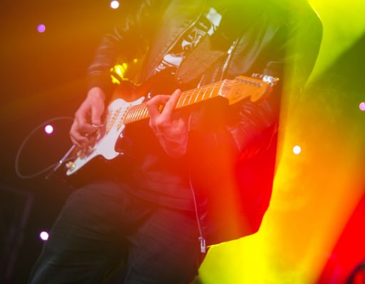 Mężczyzna gra na gitarze z oświetleniem scenicznym w tle.