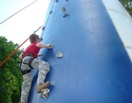 Chłopiec wspina się po dmuchanej ściance wspinaczkowej na imprezie plenerowej.
