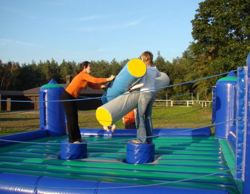 Dwie kobiety walczą na dmuchanym ringu gladiatorów na imprezie plenerowej.