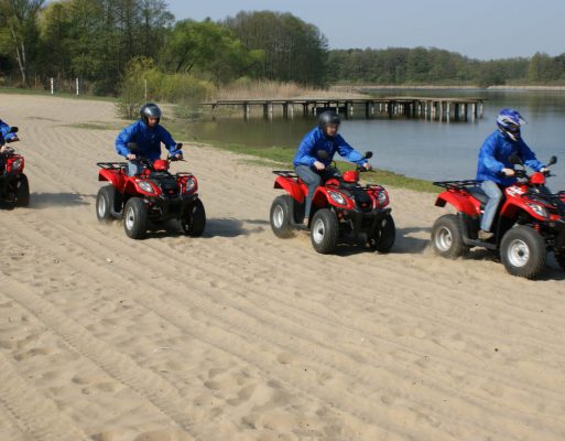 Cztery osoby jadą quadami po plaży w czasie imprezy firmowej.