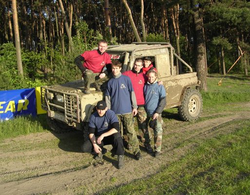 Grupa ludzi stoi przy samochodzie do jazdy offroad w czasie imprezy firmowej.