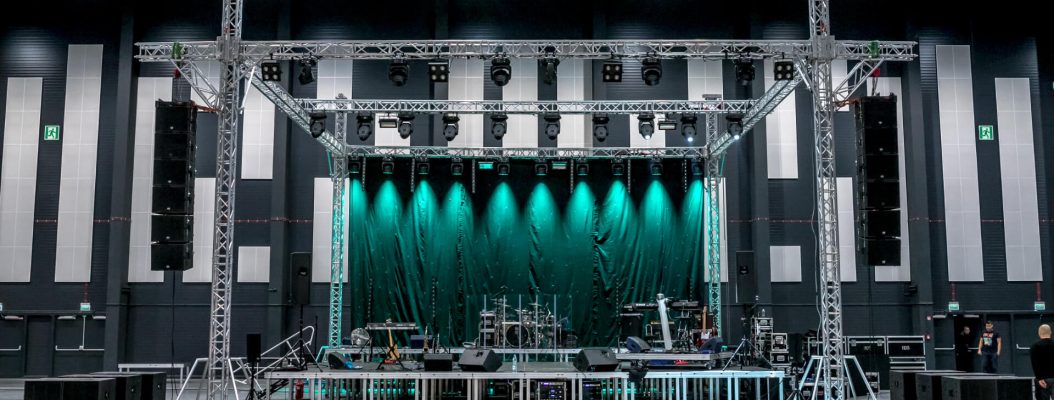 Duża scena ze sprzętem do nagłośnienia, oświetlenia i instrumentami stoli w hali targowej.