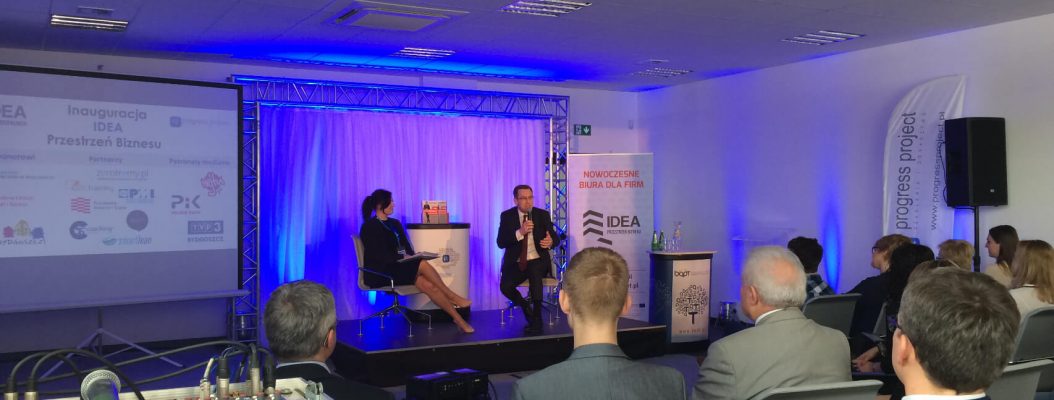 Kobieta i mężczyzna siedzą na podeście scenicznym na konferencji.