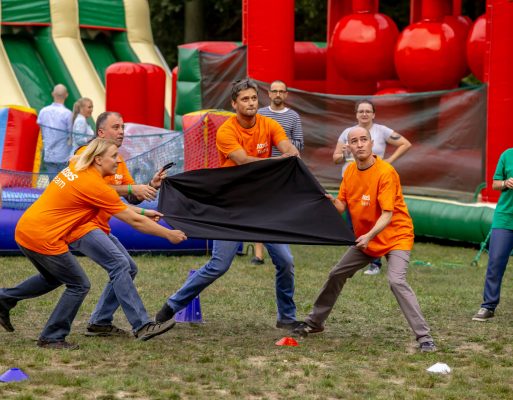 Cztery osoby trzymają kawałek materiału w trakcie konkurencji na integracji firmowej w plenerze.