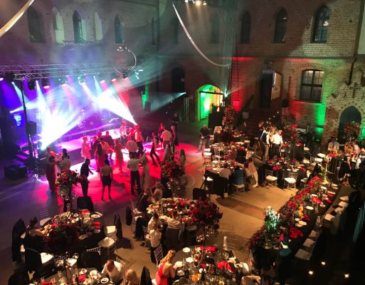 Zabawa na parkiecie przed kolorowo oświetloną sceną na weselu.