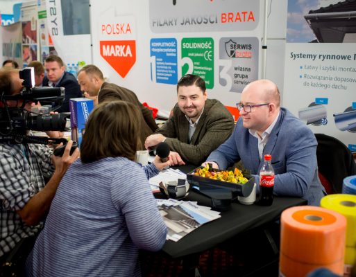 Kobieta prowadzi wywiad z dwoma mężczyznami w trakcie targów.