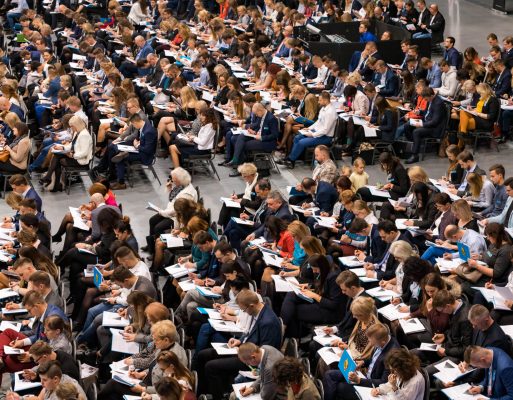 Ludzie siedzący na krzesłach przygotowują notatki w trakcie konferencji.
