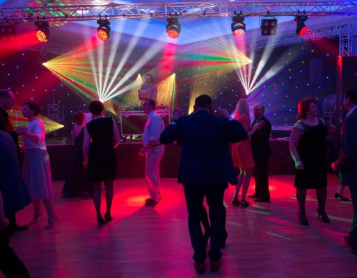 Dj stoi przy konsolecie na oświetlonej scenie w trakcie zabawy na prywatnej imprezie.