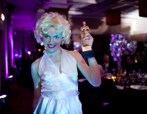 Kobieta przebrana za Marylin Monroe trzyma w ręce statuetkę Oscara na imprezie integracyjnej.